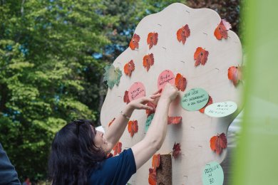 Eigene Ideen einbringen_Beteiligung Eine Frau pinnt Vorschläge an einen Ideenbaum