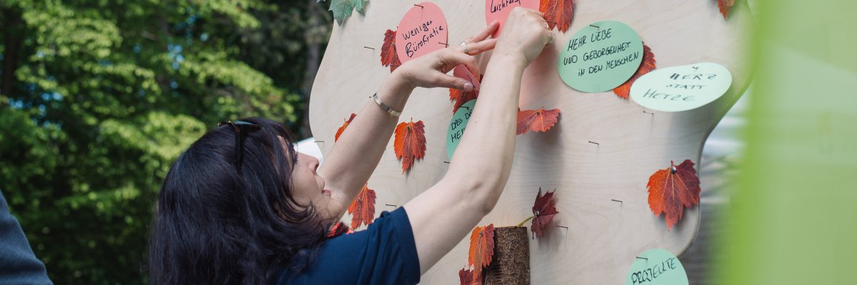 Eigene Ideen einbringen_Beteiligung Eine Frau pinnt Vorschläge an einen Ideenbaum