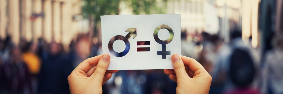 Eine Person hält ein Schild mit den Symbolen für die Geschlechter und einem Gleich-Zeichen hoch.