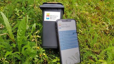 Eine kleine Mülltonne und Handy liegen im Gras