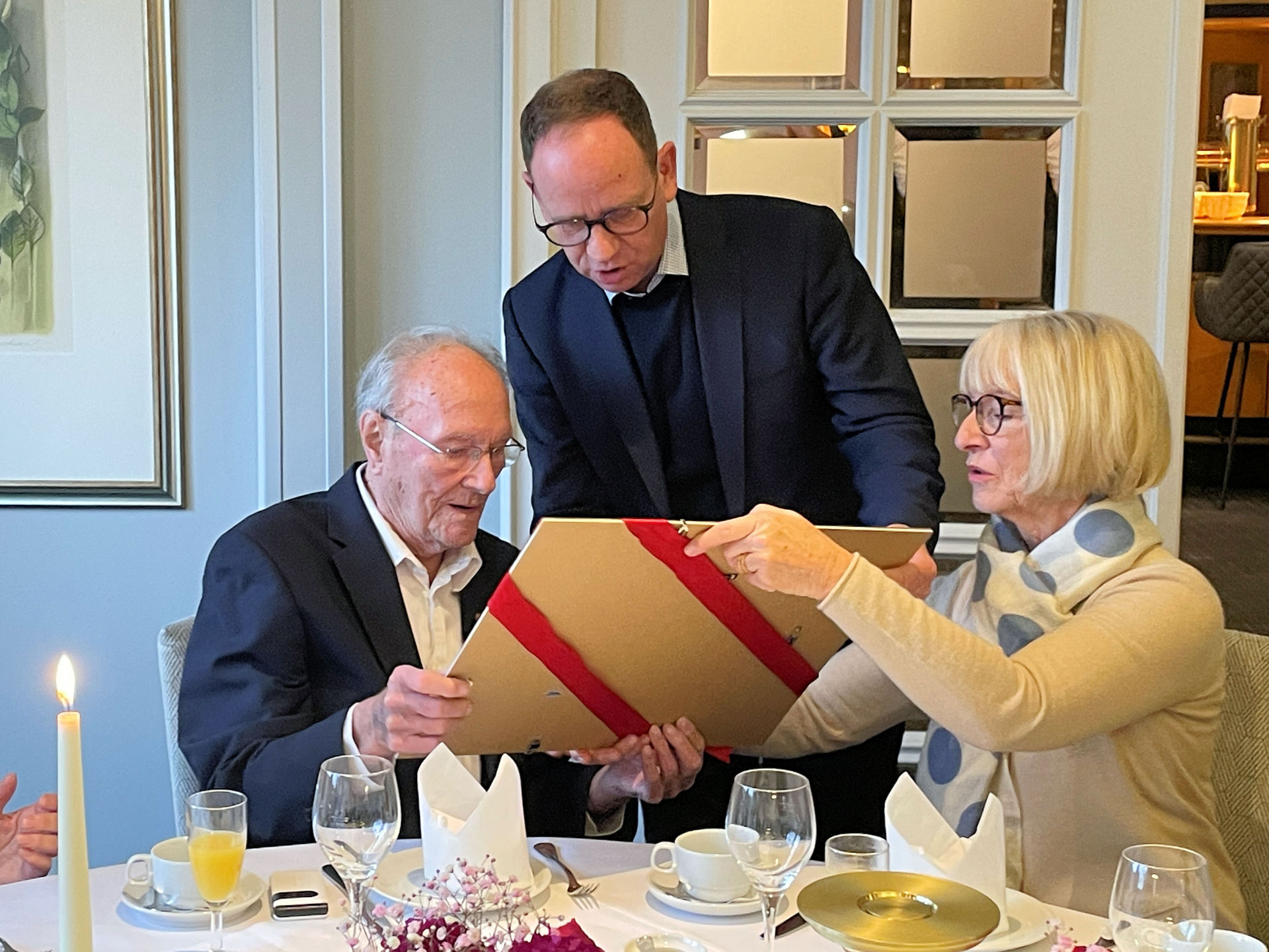 Bürgermeister Peter Kock überreicht Heinz Röthemeier zu seinem 102. Geburtstag eine Foto-Collage. Rechts seine Tochter Claudia Röthemeier.