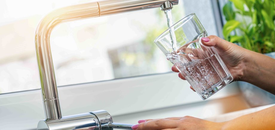 Eine Frau füllt ein Glas mit Trinkwasser am Wasserhahn.