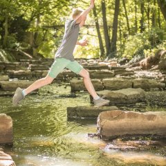 Kind springt über Steine in der Bastau