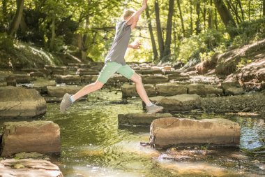 Kind springt über Steine in der Bastau